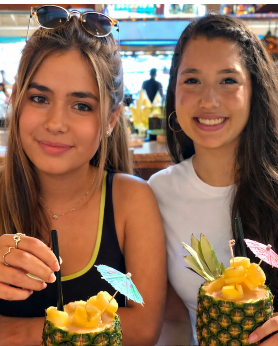 Two women holding pineapple cocktails in a casual setting